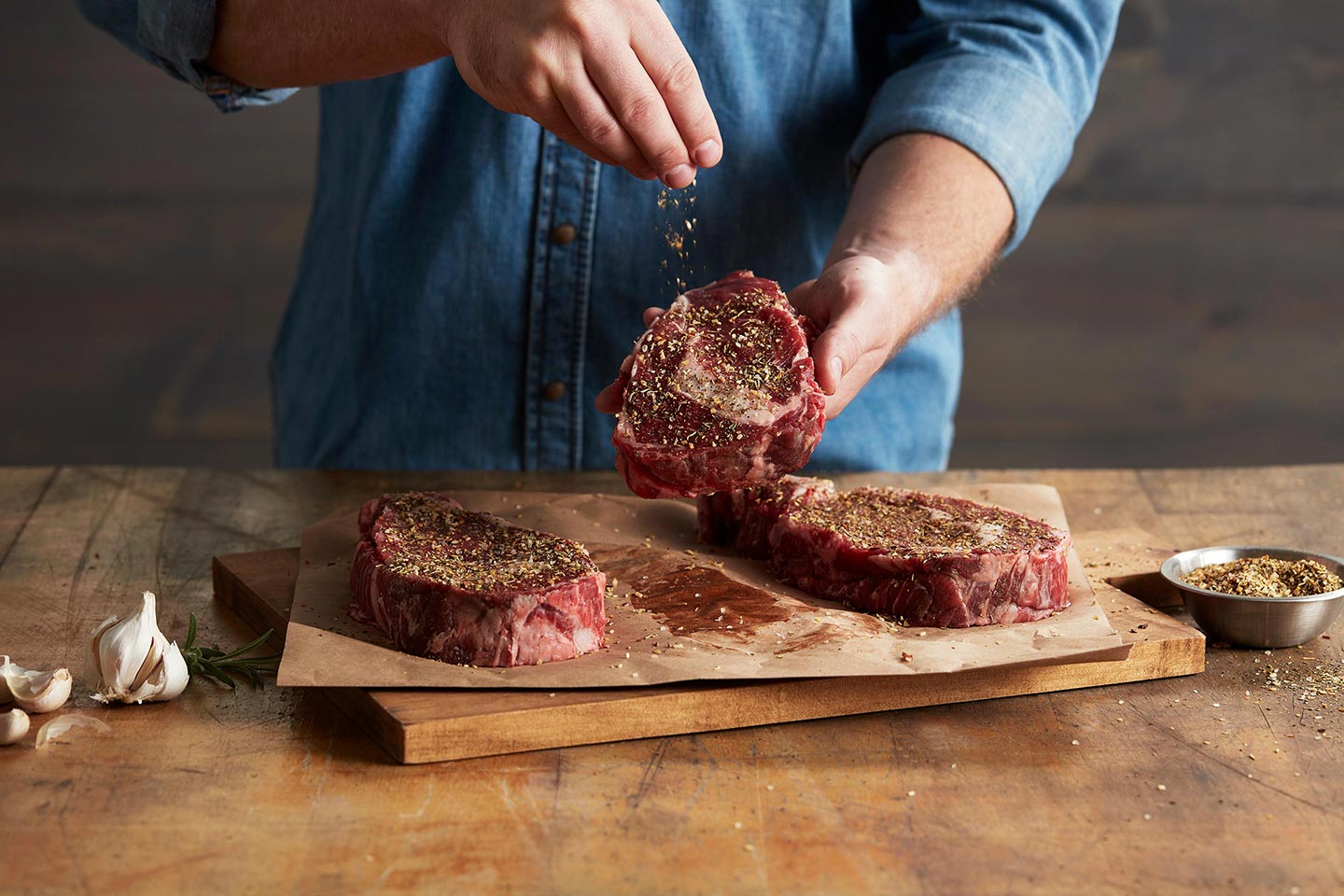 Hand sprinkling Twist'd Q seasoning on steak sitting on cutting board.