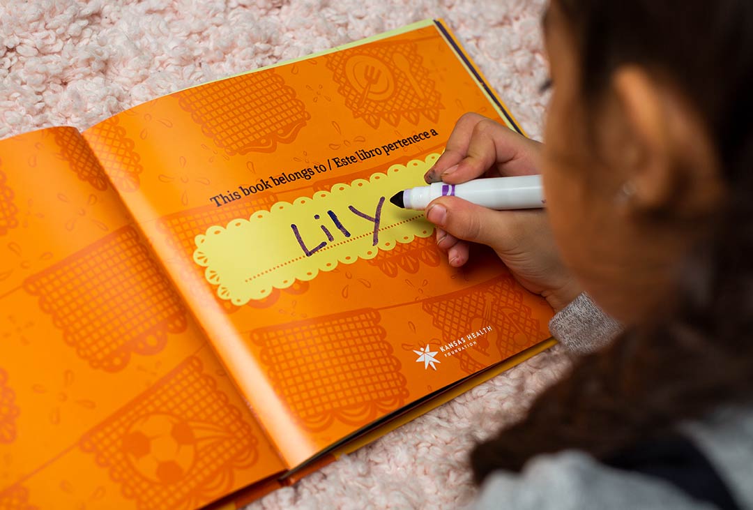 Child writing her name in the Just Like You book inside cover.