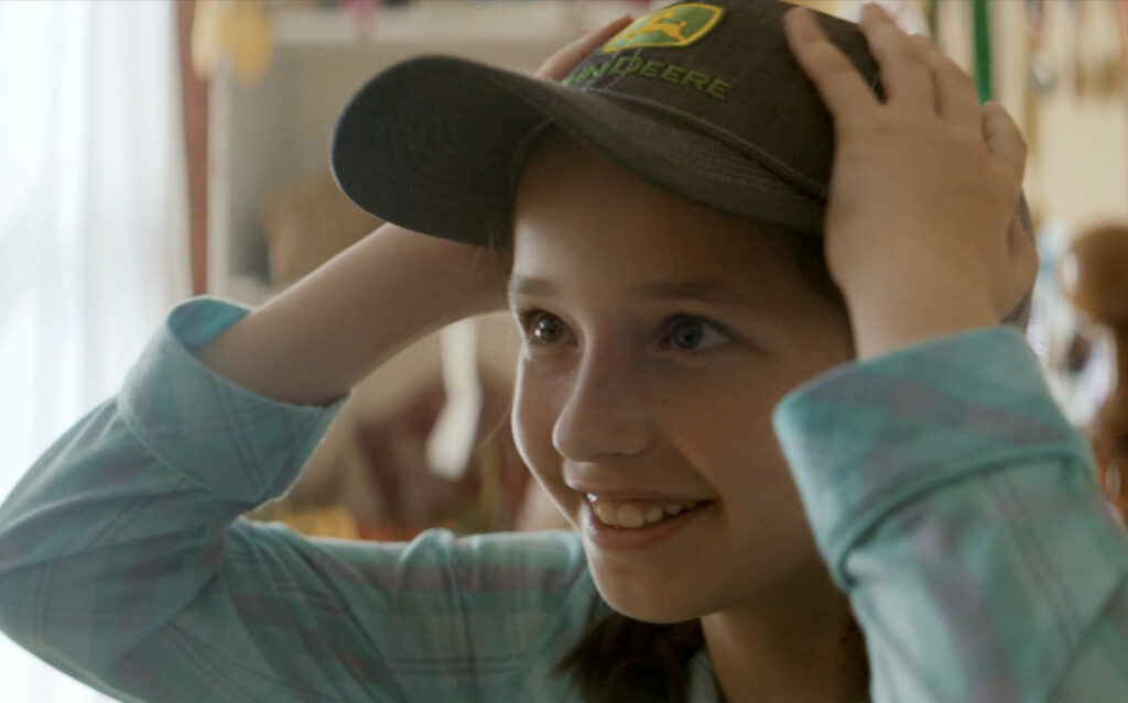 Young girl putting on a green John Deere ball cap.