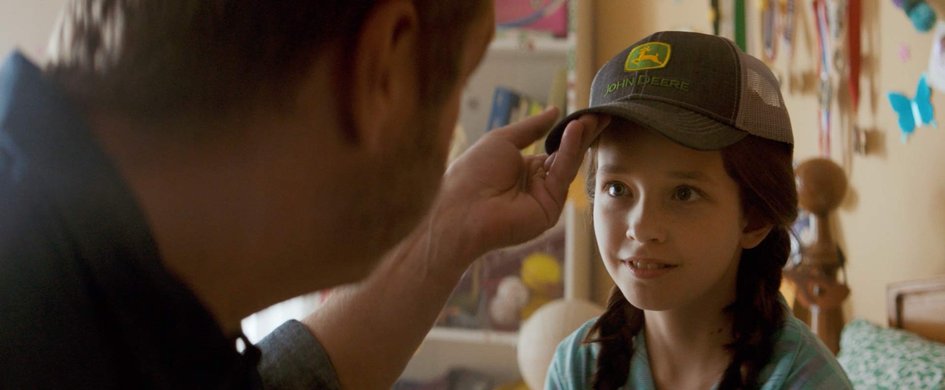 Dad places John Deere cap on young girl's head