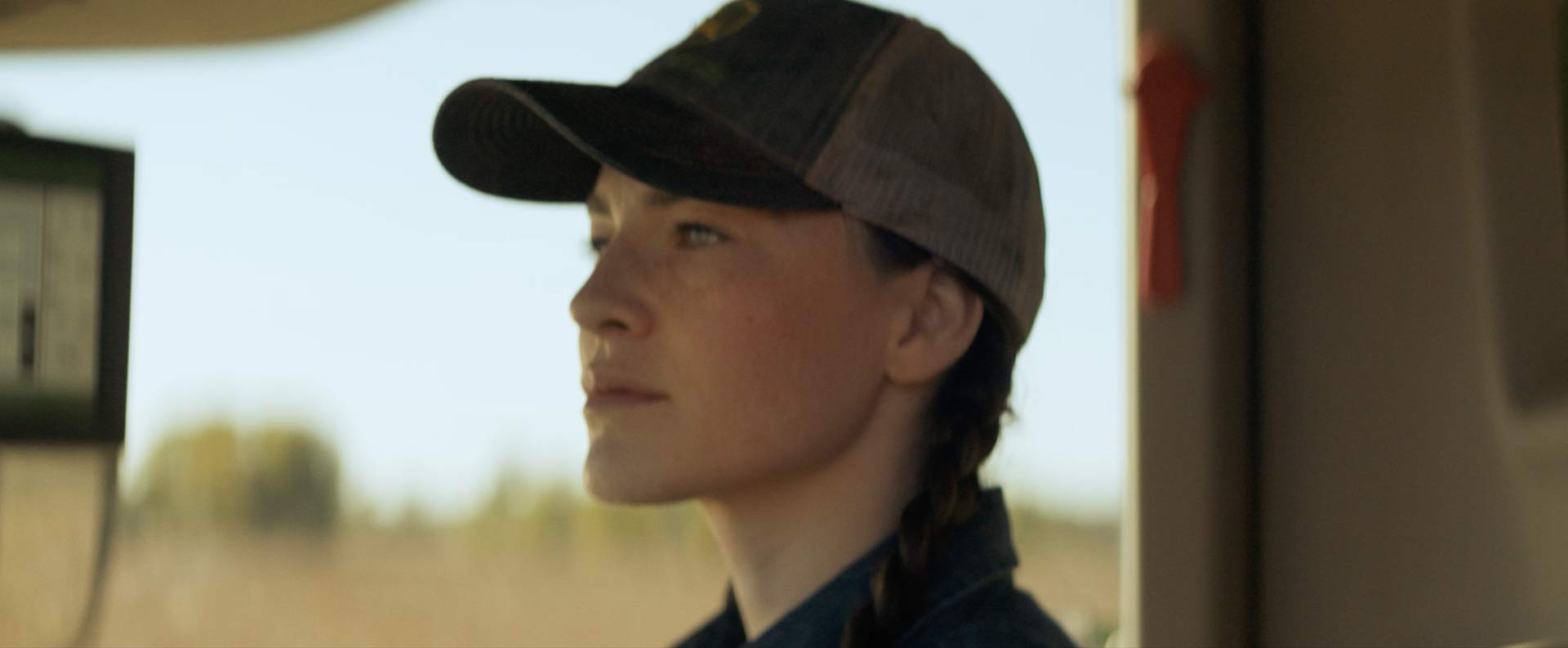 Close up of young 20-ish woman wearing John Deere cap driving a combine