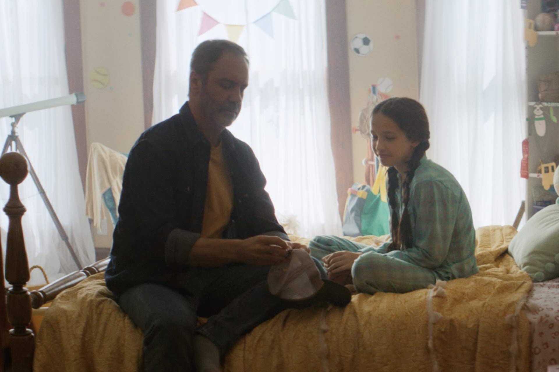 Young girl and her father sit on the bed in her room as they chat.