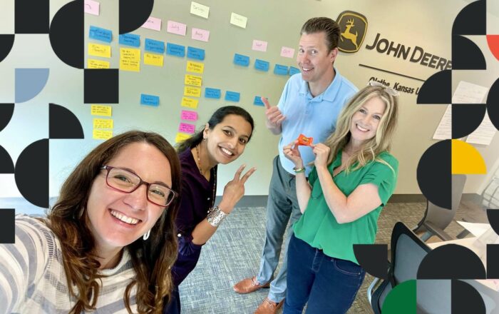 Amanda Hembree with people from a John Deere training session standing in front of a wall of post-it notes – all smiling and looking at the camera