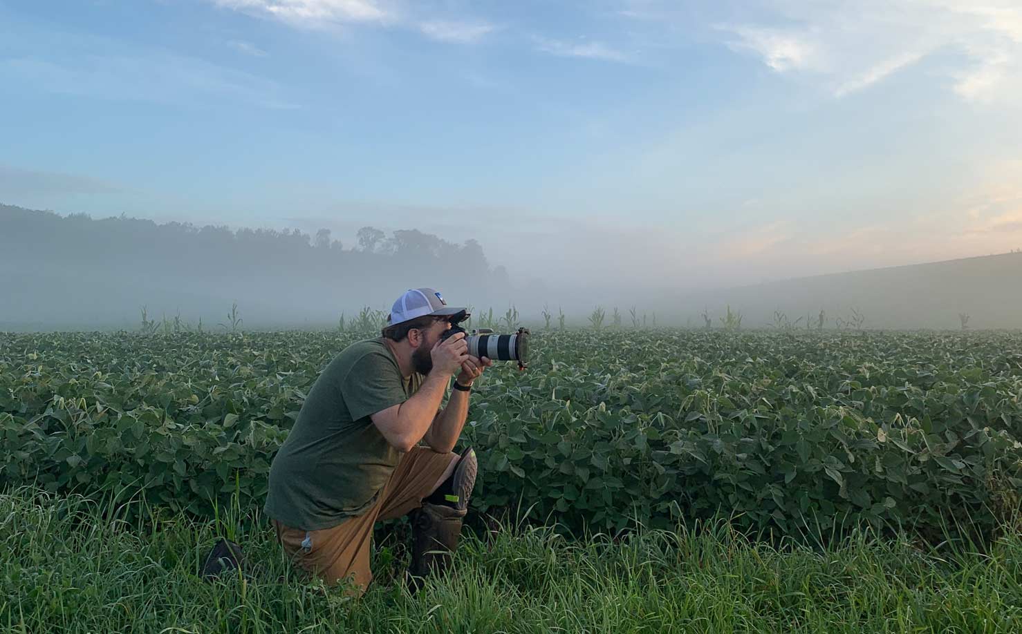 Kneeling photographer taking a photo in a misty farm field