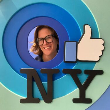 Beth Wickerson looking through a circular cutout that has the Facebook thumbs up icon and the letters NY
