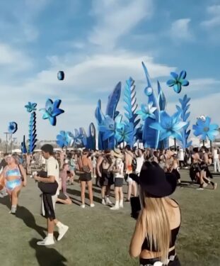 Crowd of people outdoors at Coachella with a garden of fanciful shapes towering behind them.