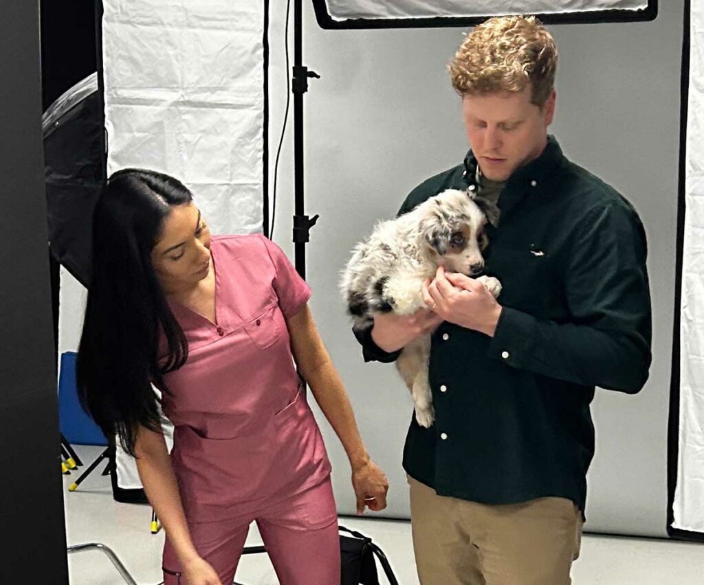Signal Theory art director holding a puppy on set while a trainer leans in to check the puppy.