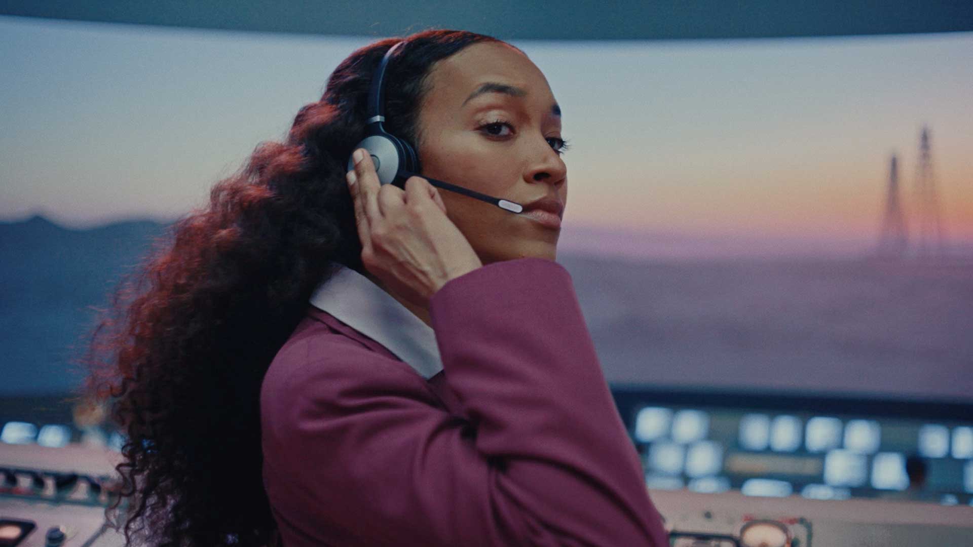 Still from John Deere's All Kinds of Fields spot of Maya wearing a headset in front of a rocket launch site mission control.