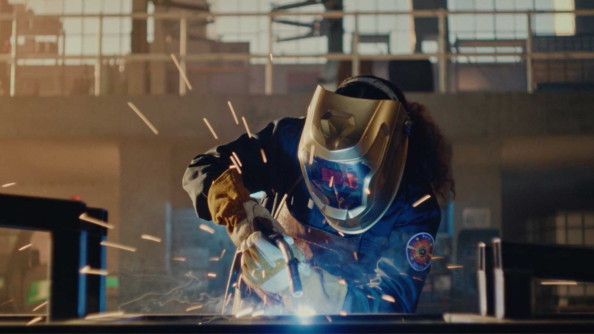 Still from John Deere's All Kinds of Fields spot of Maya welding with sparks flying in an industrial setting