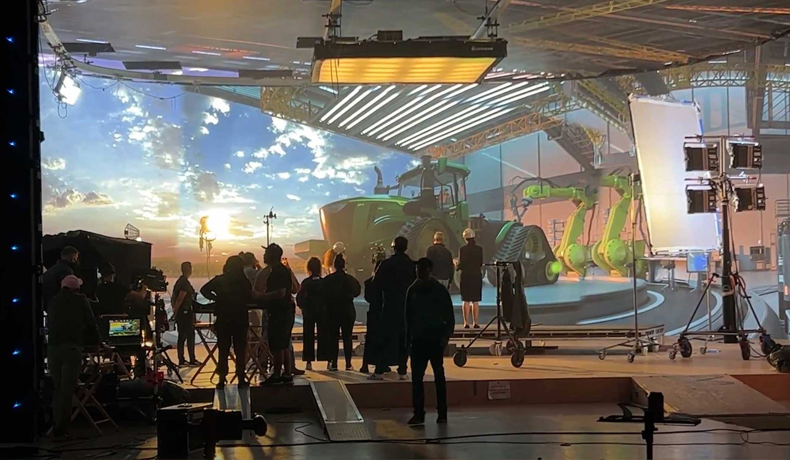 Behind the scenes view shooting on Volume stage with a large John Deere tractor in the background and many crew member silhouetted in the foreground.
